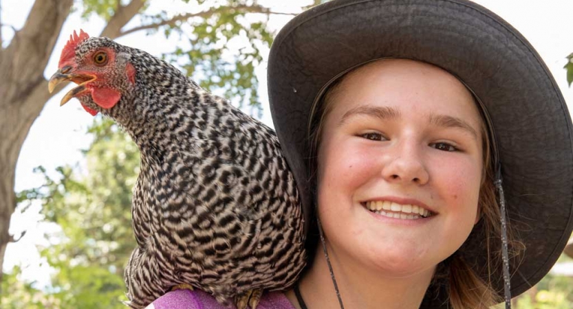 a person with a chicken on their should smiles at the camera during a service project with outward bound